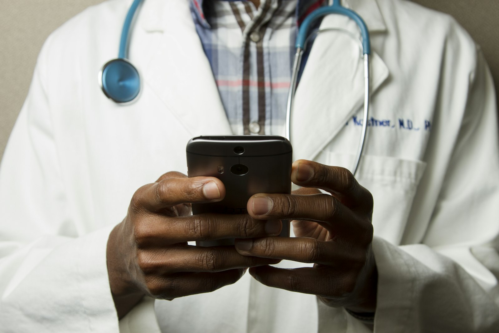 Sundhedsfaglig med blåt stetoskop der holder en telefon i hænderne